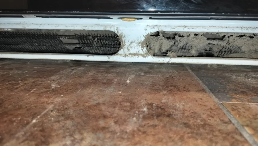 Debris accumulation across a refrigerator condenser intake during inspection.