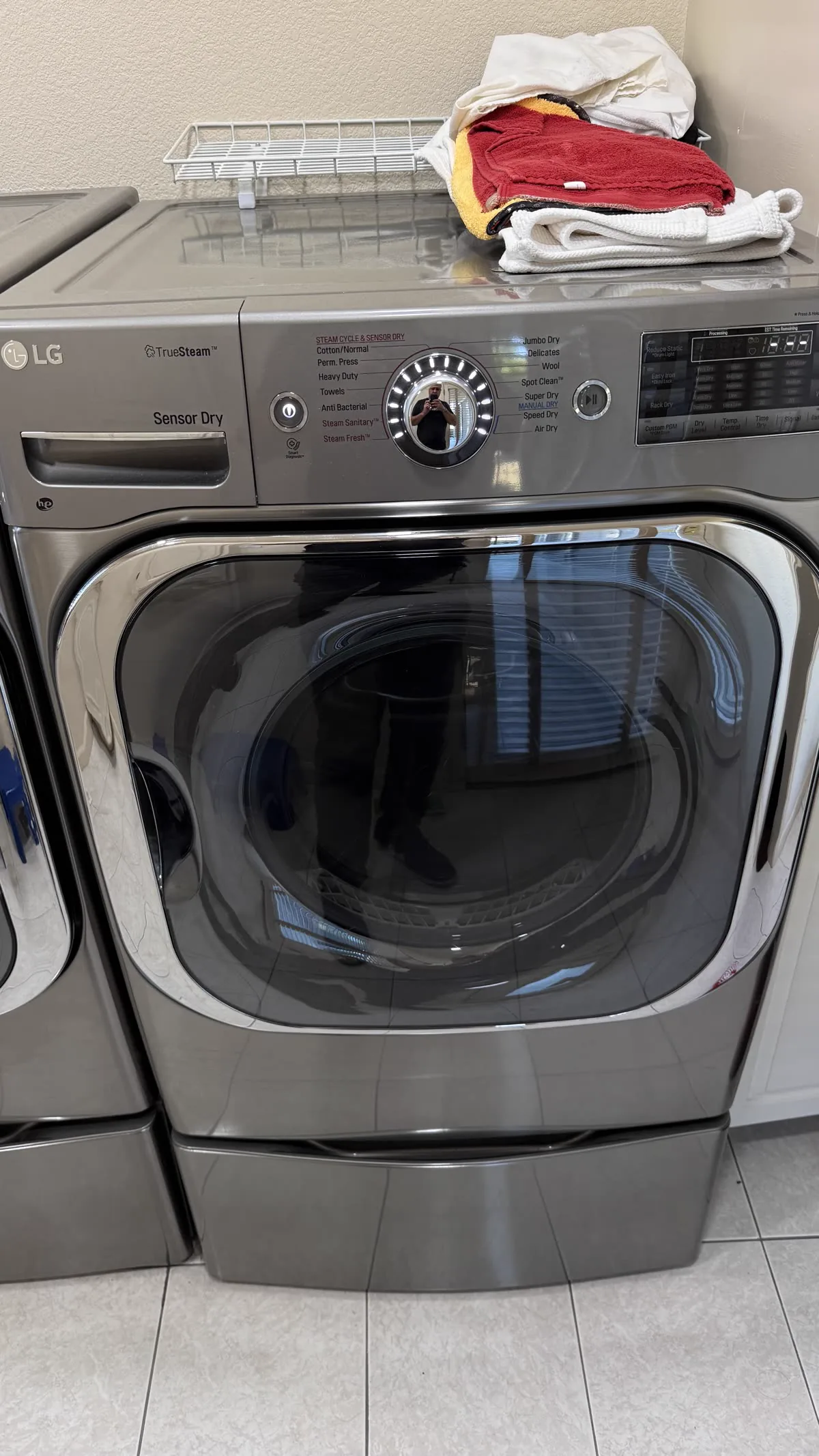 LG front-load dryer on a pedestal in a home laundry room.