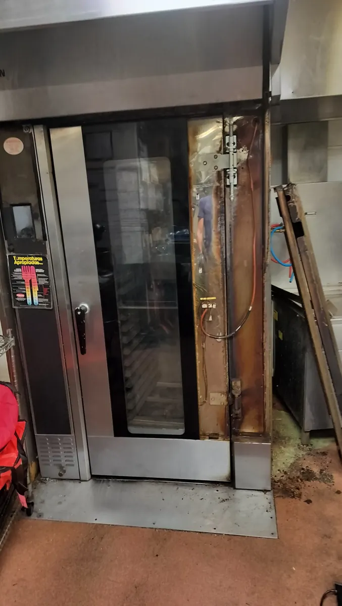 Commercial bakery rack oven with the door-hinge area exposed during service access.