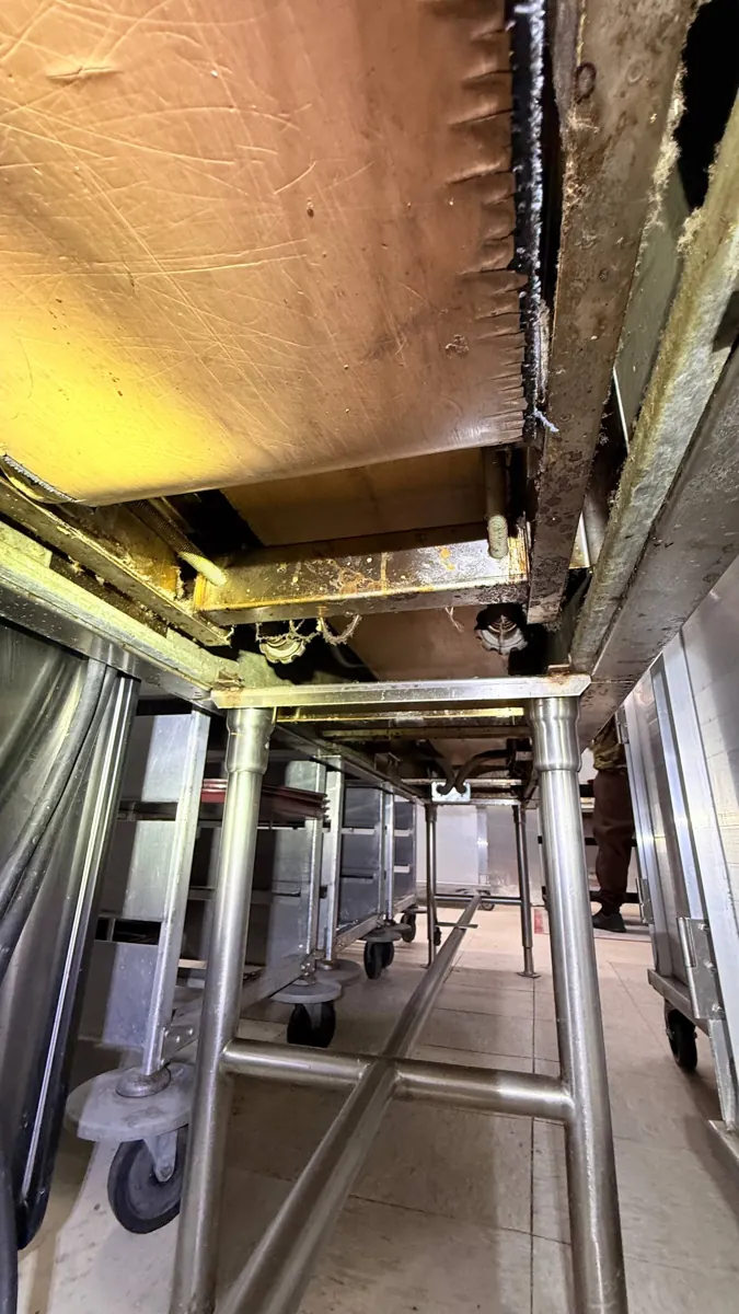 Underside of a commercial tray conveyor showing the belt edge, return path and support frame.