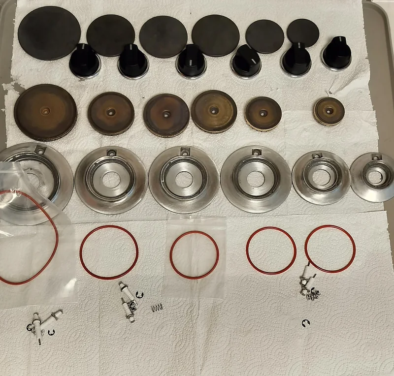 Viking burner caps, knobs, brass-colored heads and silver bases arranged in rows with orange seals and ignition components on a workbench