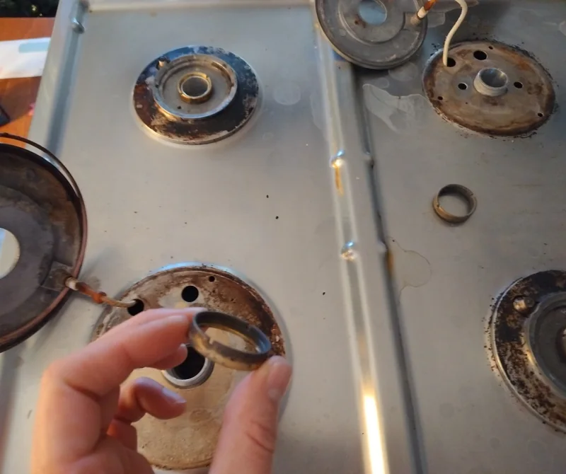 Disassembled Viking gas cooktop with lifted burner bases, attached ignition electrodes and a metal retaining ring held for inspection