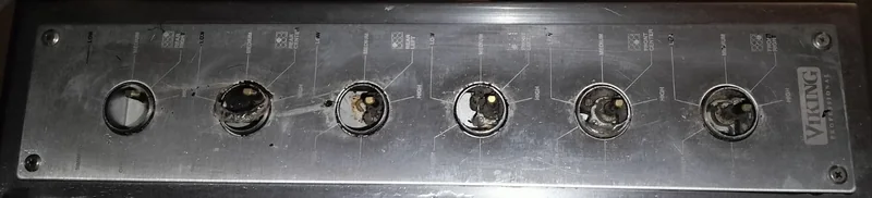 Viking stainless control strip with all six knobs removed and patchy printed burner markings