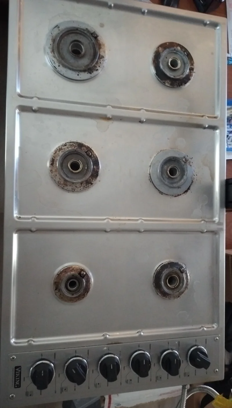 Six-burner Viking gas cooktop with grates and burner caps removed and deposits visible around the exposed bases