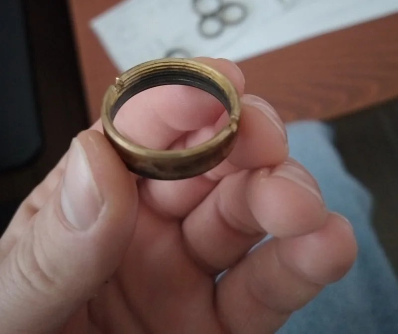 Close-up of a threaded brass-colored burner retaining ring held for inspection